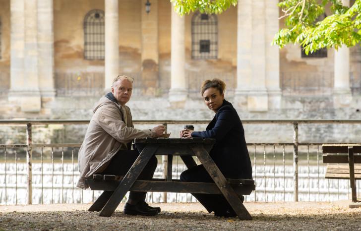 Jason Watkins et Tala Gouveia, assis face à face à une table de pique-nique, regardent l'objectif